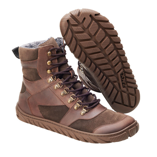 The brown EXPLORER Waterproof boots from ZAQQ are high leather shoes with dark laces and gold eyelets. Ideal for outdoor adventures, they have a sturdy, textured sole for excellent grip. One boot is pictured upright to show the side profile, while the other is angled to highlight the sole design.
