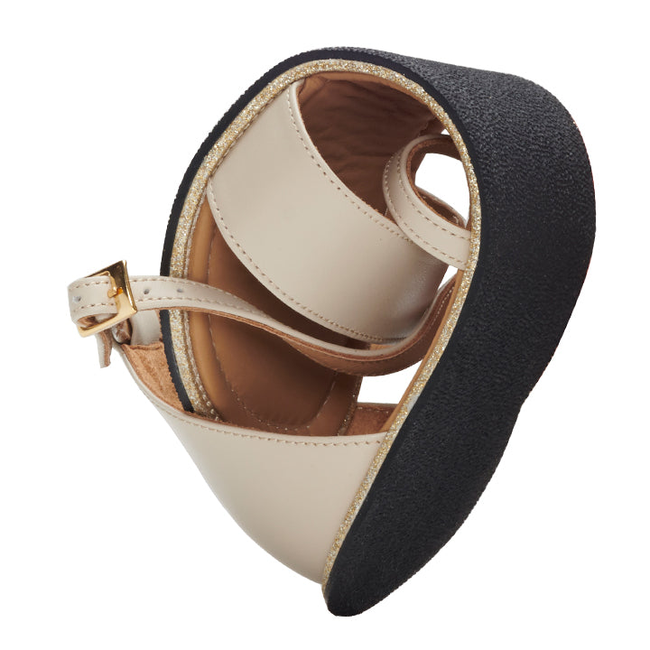 Close-up of the QEEP Beige shoe from ZAQQ, made from supple nappa leather. It features a black textured sole and gold detailing secured by a small buckle strap. The shoe is rolled compactly and shows its flexibility and comfort similar to that of a barefoot sandal.