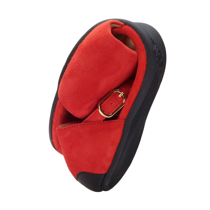 Introducing TEQA Red from ZAQQ: These velvety red shoes feature a smooth black rubber sole and an elegant gold buckle with a simple heel. Inspired by chic barefoot shoes, this design highlights both the unique style and flexibility of the footwear.