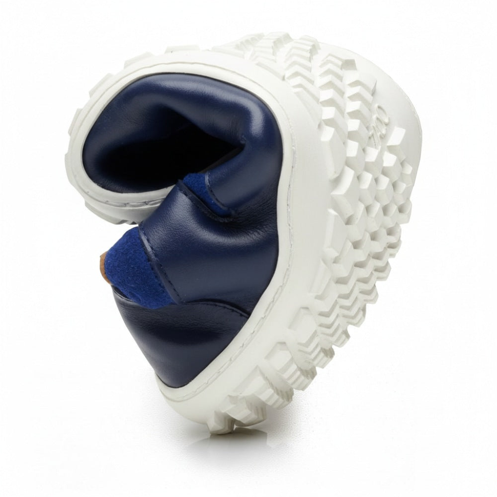 The image shows a close-up of the SHOQQ Trident from ZAQQ, which features a navy and white design with a chunky, textured sole made from durable rubber that is twisted to highlight its flexibility. The upper of the shoe is smooth and made of nappa leather-like material, which forms an ideal contrast to the robust sole.