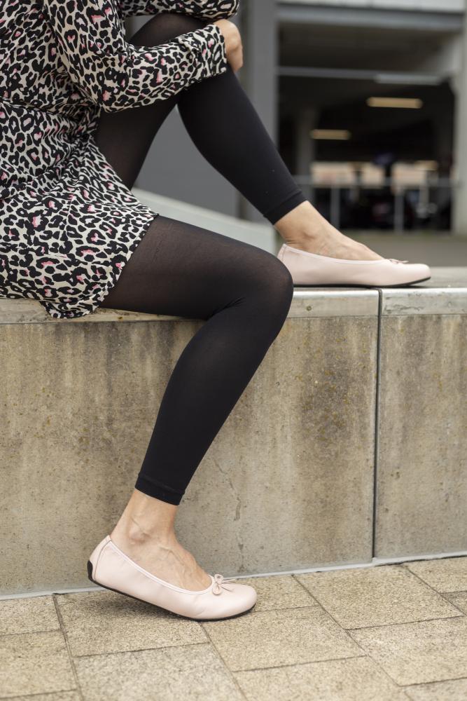 A person sits comfortably on a concrete ledge wearing a leopard print dress, black leggings and LOOQ nude shoes ZAQQ. The outfit exudes effortless elegance against the backdrop of an urban outdoor space.
