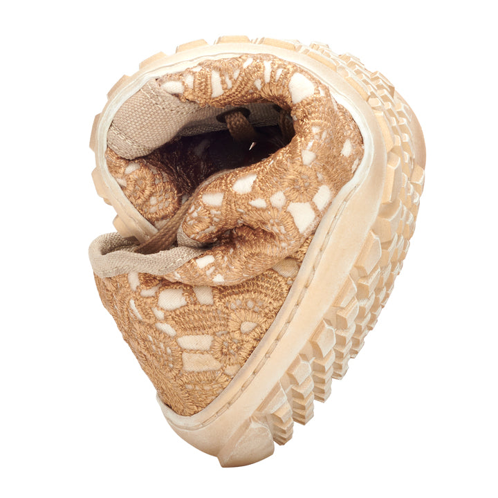 The QELLY Beige Gold Sneaker from ZAQQ with a tan and beige crochet design and a thick, sturdy sole is curved in the middle to demonstrate its freedom of movement. The barefoot shoe stands on a white background.