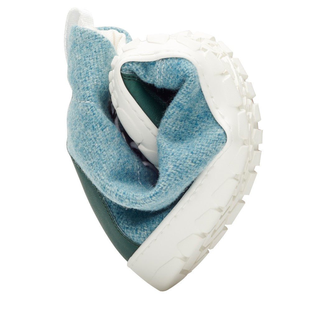 The QICE Green from ZAQQ is elegantly twisted into a heart shape, which underlines its flexibility. This barefoot shoe features a white textured outdoor rubber sole and an upper that combines blue fabric with green material.
