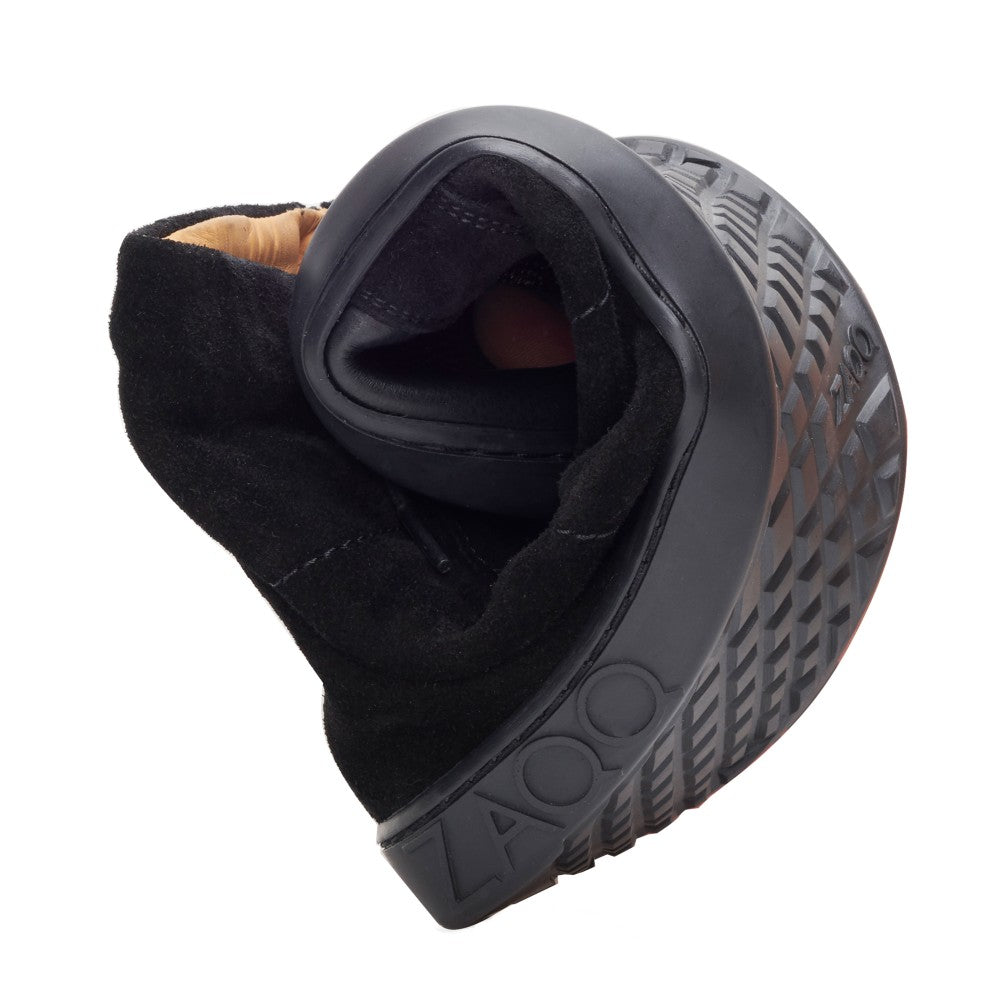A single QORE High Black flexible sneaker-style shoe is folded in half to highlight its flexibility. The sole features a textured pattern and the brand name ZAQQ is stamped on the side. The interior is lined with beige suede.