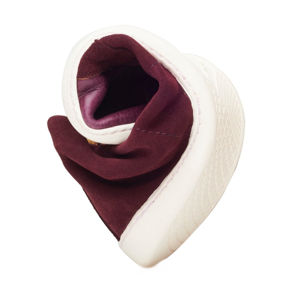 The QORE Mid Mazarine from ZAQQ is a white, mid-cut sneaker with a thick sole that is artfully folded in a spiral shape to reveal its maroon interior. The material of the shoe appears soft and flexible and emphasizes the long-term cushioning and distinctive design of this versatile footwear.