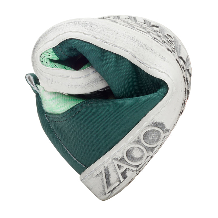 A flexible sneaker in green and white, twisted into a loop that exposes the sole and part of the inner material. The brand name is in the heel area ZAQQ engraved showcasing the barefoot shoe design. This is the QRIS Green model.