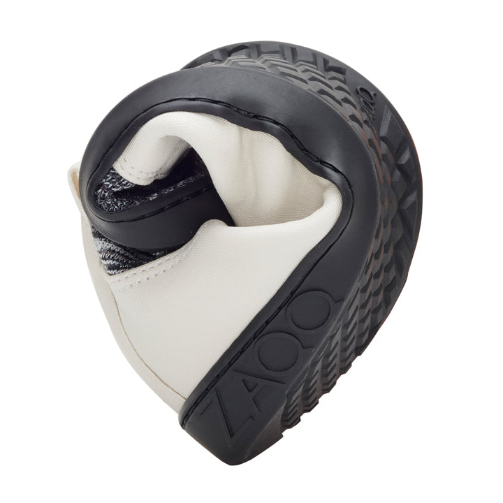 A close-up of the QRIS Gray sneaker from ZAQQ features a dramatic curve that highlights its flexibility. The brand name is visible on the textured rubber sole. The shoe is made from both smooth and textured materials in a sleek black and white design.