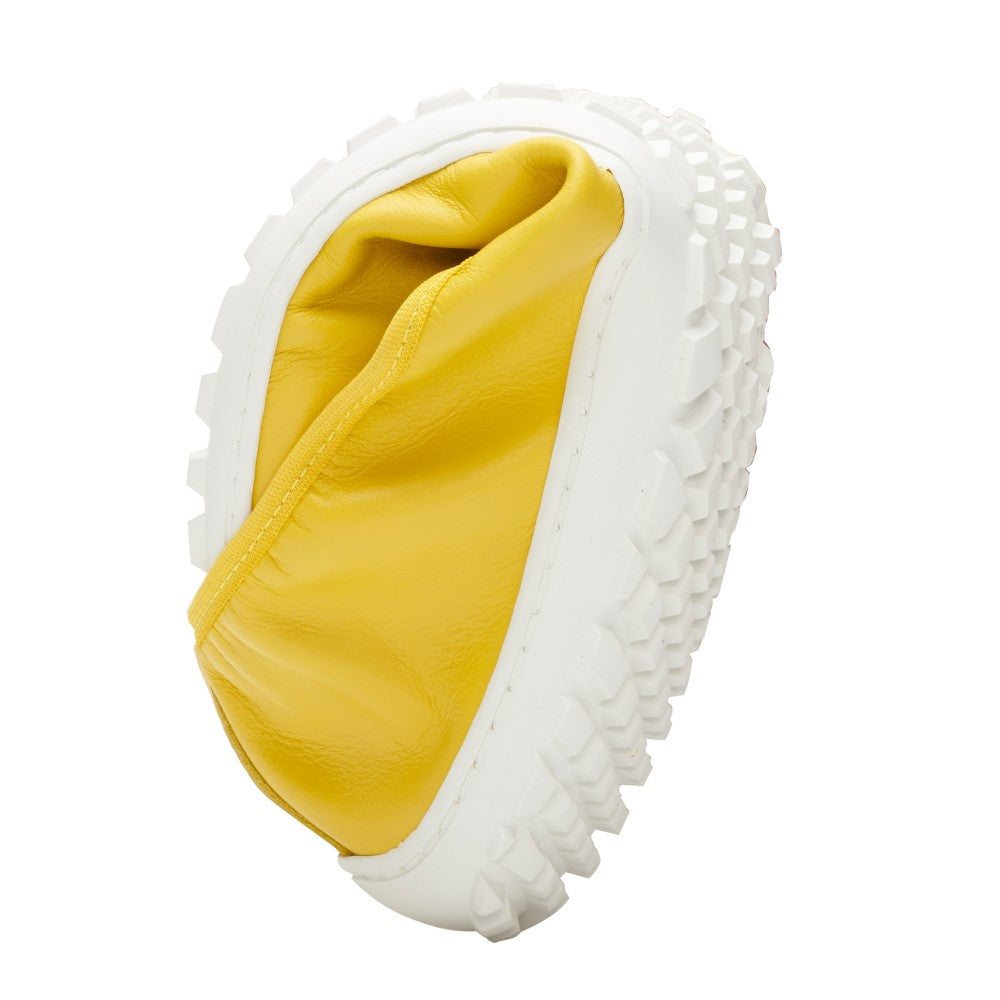 A SUQAR Lemon from ZAQQ, with a yellow, wrinkled object embedded in a white, textured surface that imitates the flexibility of nappa leather. The design reflects an artistic or abstract aesthetic similar to a barefoot shoe.