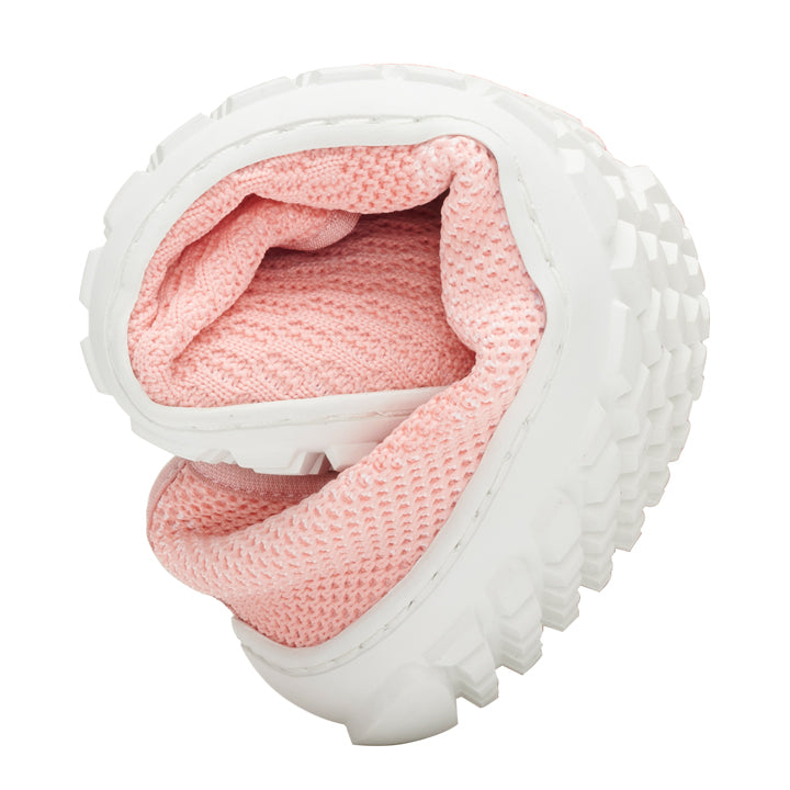 The light pink SUQAR sneaker from ZAQQ is presented rolled up to highlight its flexibility. It is made from cotton knit fabric and has a visible textured white rubber sole on the outside.
