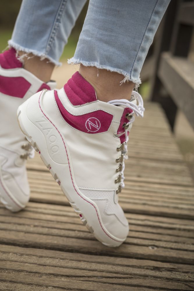 A person who ZAQQ Wearing VAQATION Pink Waterproof Boots, paired with light blue jeans with frayed hems, stands confidently on a wooden surface.