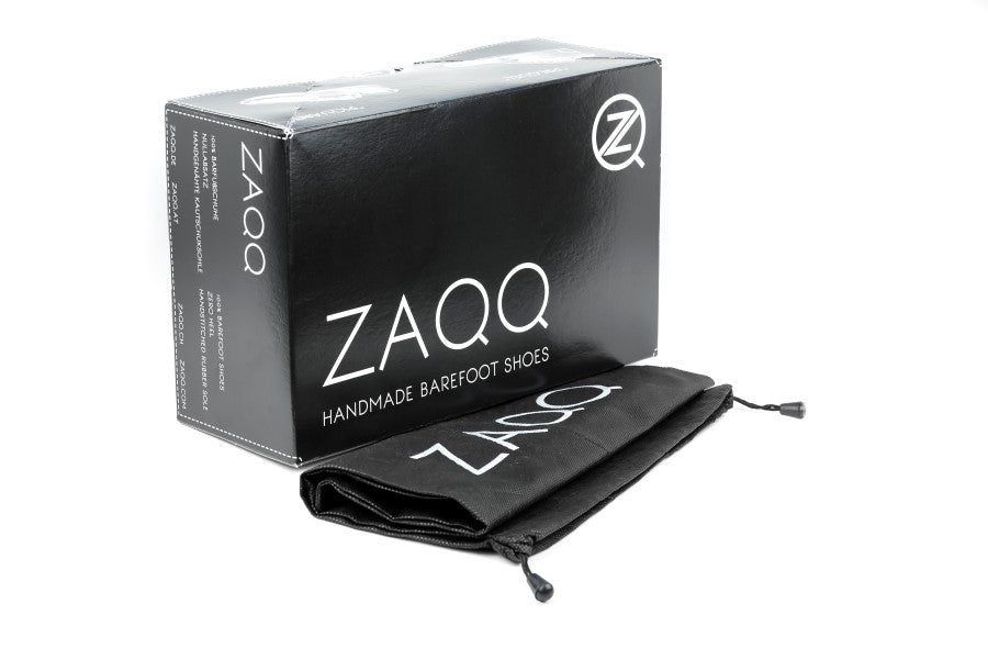 A CLIQ Nude shoe box from ZAQQ in black with white lettering “Handmade Barefoot Shoes” is presented together with a matching black bag. The bag decorated with the ZAQQ Logo and equipped with a drawstring closure, is perfect for your CLIQ shoes or strappy sandals.