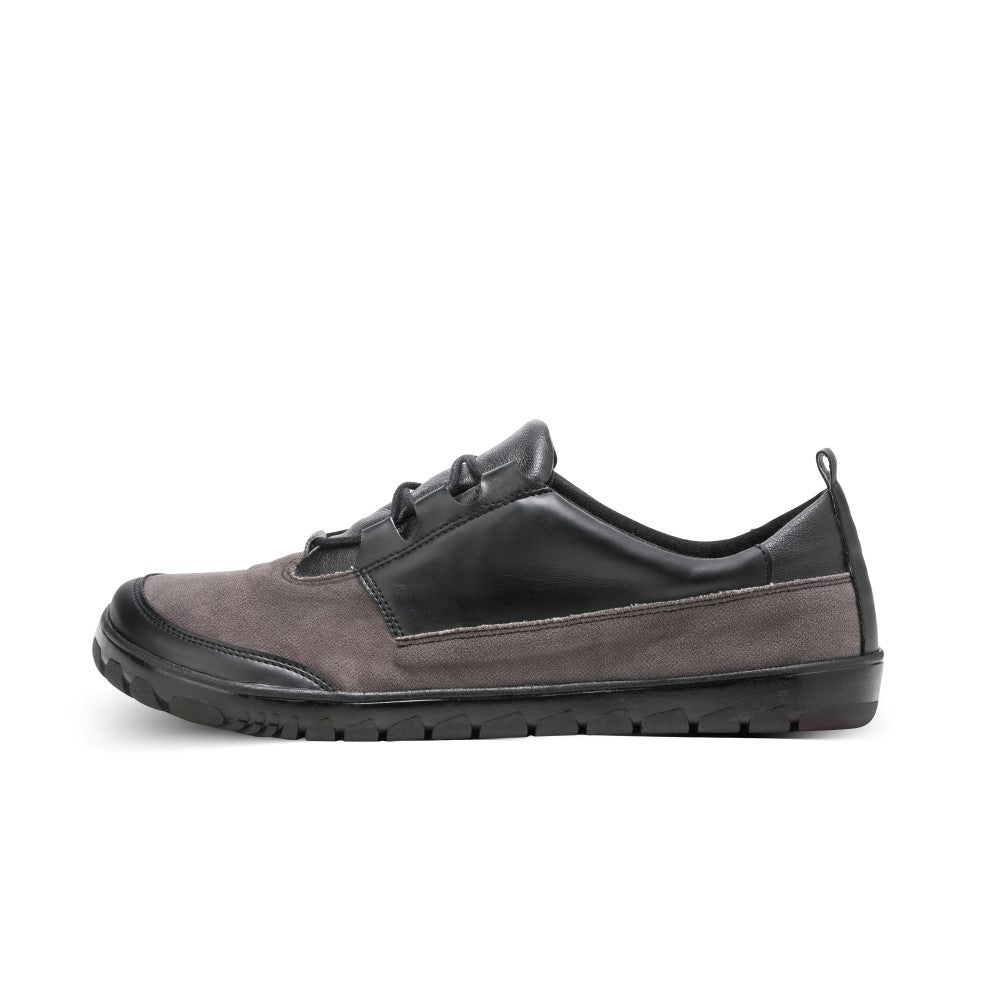 The QUEST Low Black Waterproof shoe from ZAQQ features an elegant side view design, with a gray suede front, a black leather accent on the side and a black sole. This minimalist footwear is waterproof, making it ideal for any adventure.