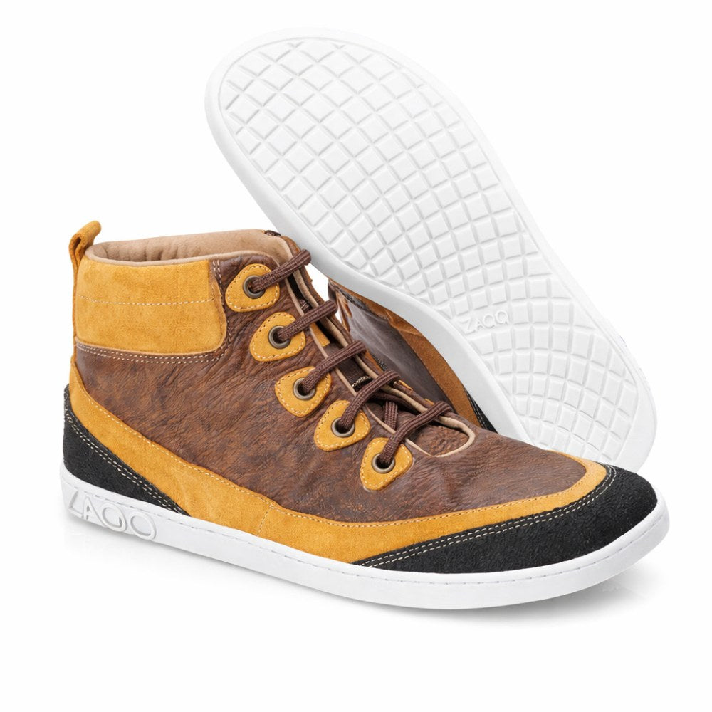 The FRANQY Brown high-top sneakers from ZAQQ offer exceptional comfort with their combination of brown leather and suede, complemented by metal eyelets and brown laces. With white rubber soles, one shoe stands upright while the other is tilted to show off its patterned sole.