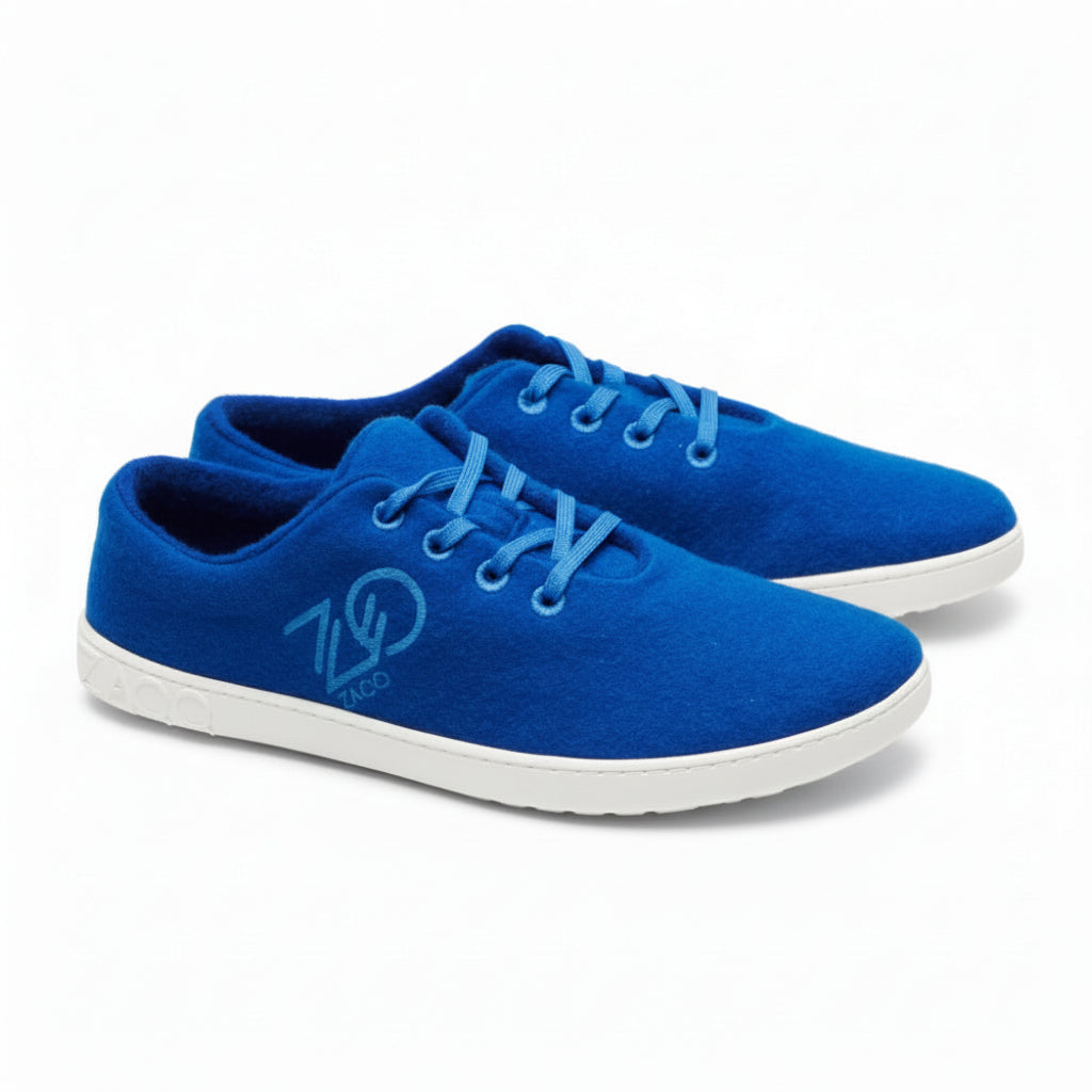 The LIQE Azur sneakers from ZAQQ Made of merino wool, they have light gray soles and blue laces. Each shoe proudly displays a circular logo with the number 700 against a simple white background, seamlessly blending comfort and style with every step.