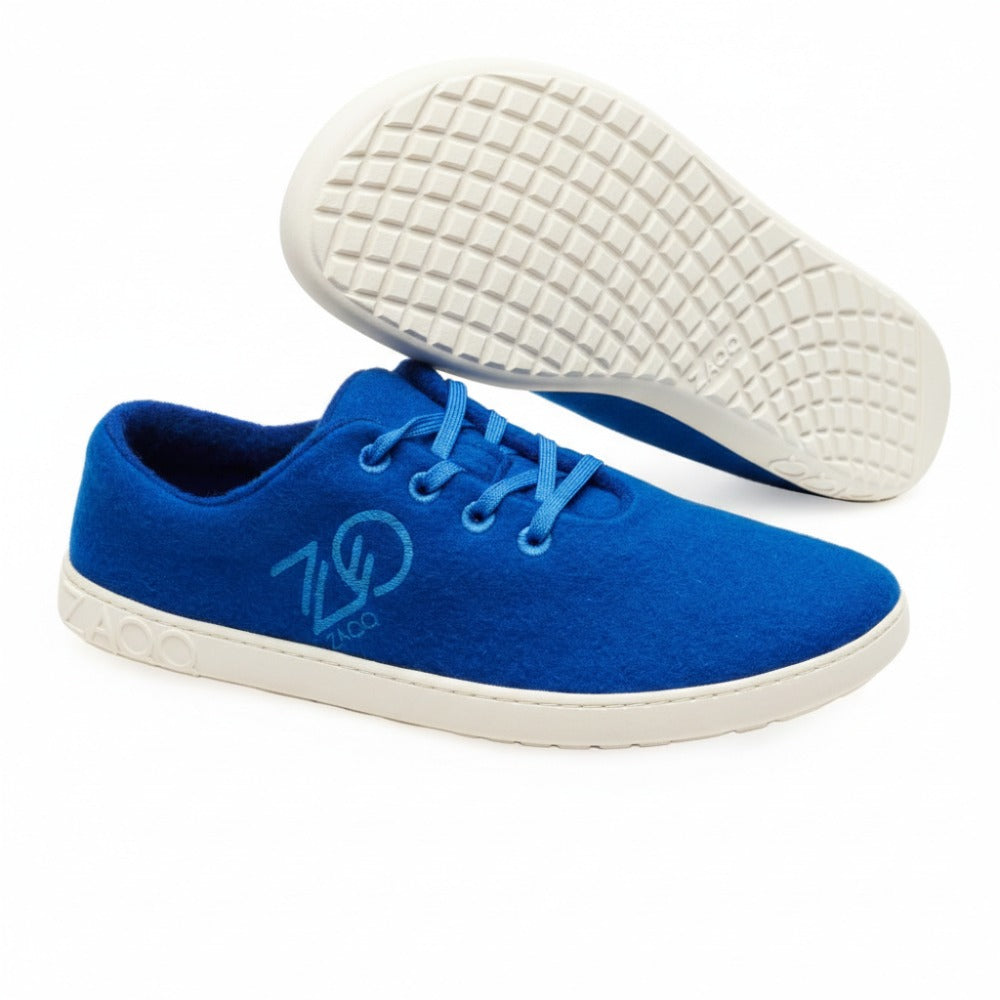 The LIQE Azur sneakers from ZAQQ are characterized by an elegant design with a blue upper and white sole, accentuated by a logo on the side. These sneakers are designed for comfort similar to barefoot shoes and feature blue laces. One sneaker is shown in a side view, while the other shows its textured sole facing forward.