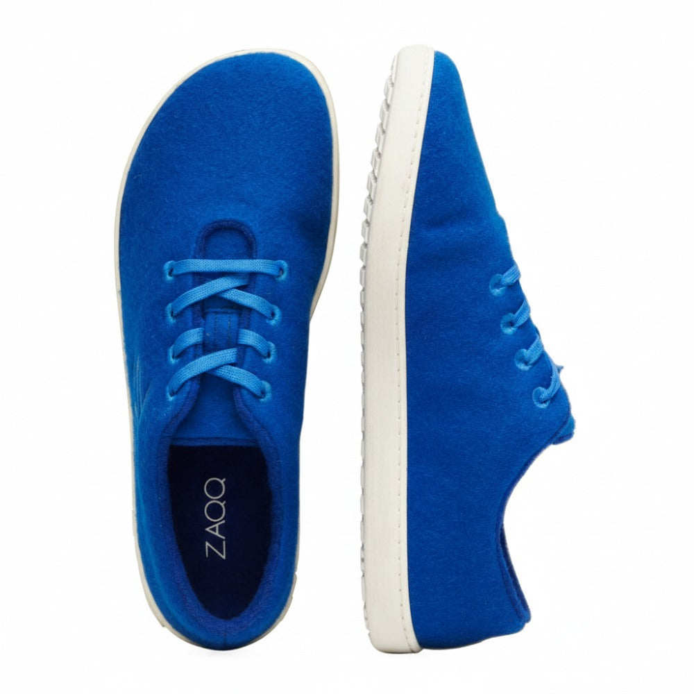 An attractive pair of LIQE Azur sneakers from ZAQQ made of merino wool shows a bright blue color, with one shoe visible from the side and the other from above. These shoes feature white soles and blue laces, while the insole of the upper shoe proudly displays their branding as a unique barefoot shoe.
