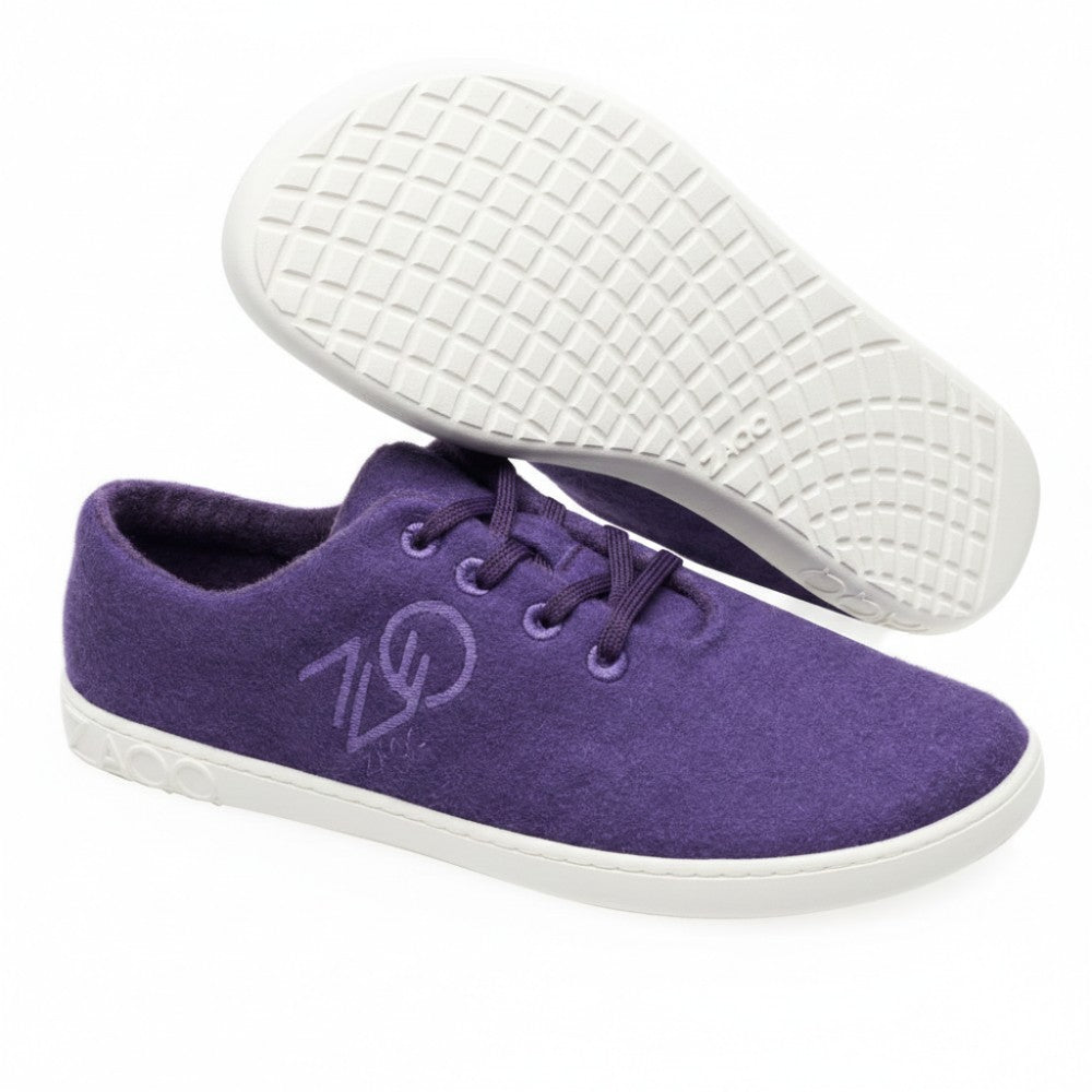 The LIQE Purple sneakers from ZAQQ offer a striking wool-like texture. The right sneaker stands upright and shows its side with the stylized ZAQQlogo, while the left one is flipped over to reveal the textured barefoot sole. Both sneakers feature gray details on the sole for an added touch of style.