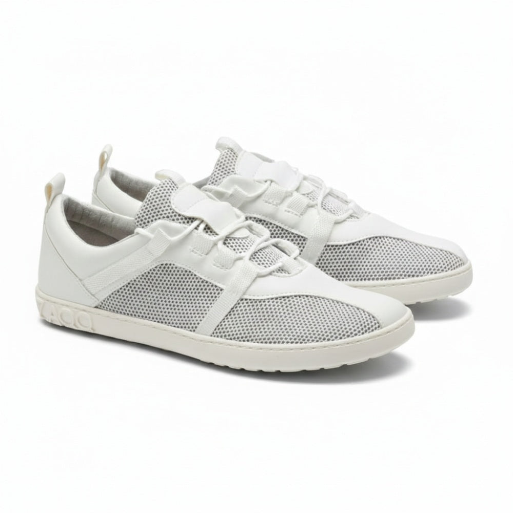 A pair of MCQARTER white sneakers from ZAQQ features breathable mesh fabric and laces on a clean white background, complemented by a gray sole with brand name embossed near the heel. These shoes are characterized by a minimalist and sporty design.