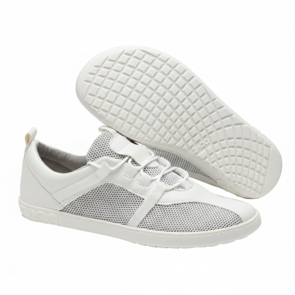 The white MCQARTER sports shoes from ZAQQ with breathable mesh details and rubber soles are issued. One shoe stands upright while the other is angled to show the profile. This highlights their precise workmanship, which offers comfort similar to that of a barefoot shoe.