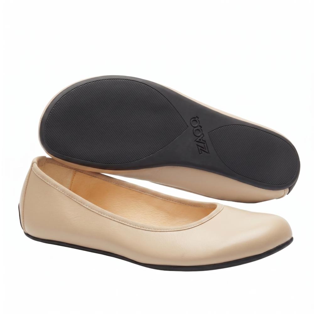 A pair of QARMA beige flats from ZAQQ has a beige nappa leather upper with black soles. One shoe stands upright, emphasizing its smooth surface, while the other is tilted to showcase the textured sole.