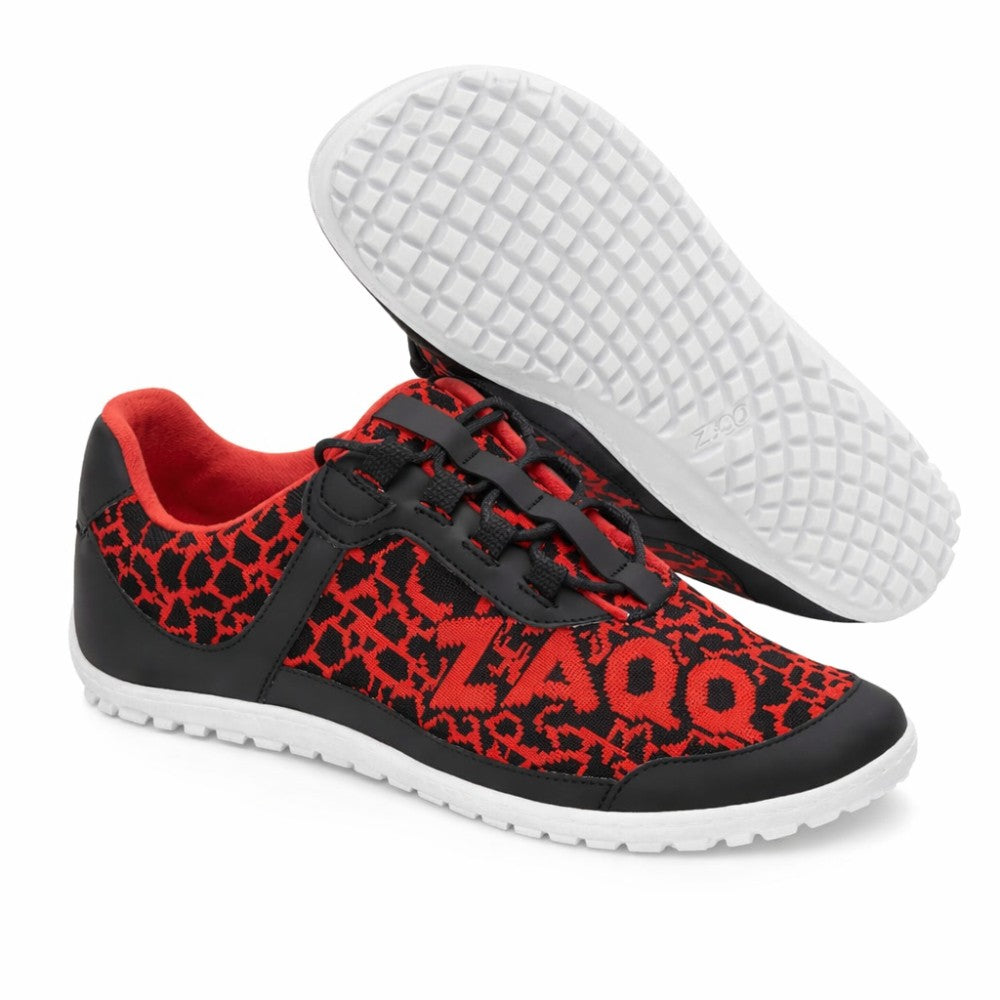 The QASEY Red sneakers from ZAQQ are made of black and red mesh fabric. These vegan barefoot shoes feature a textured design with black overlays on red and feature the brand name ZAQQ on the page. The white sole is designed to be flexible and has a rubber texture reminiscent of a grid, with a shoe so visible that its bottom can be seen.
