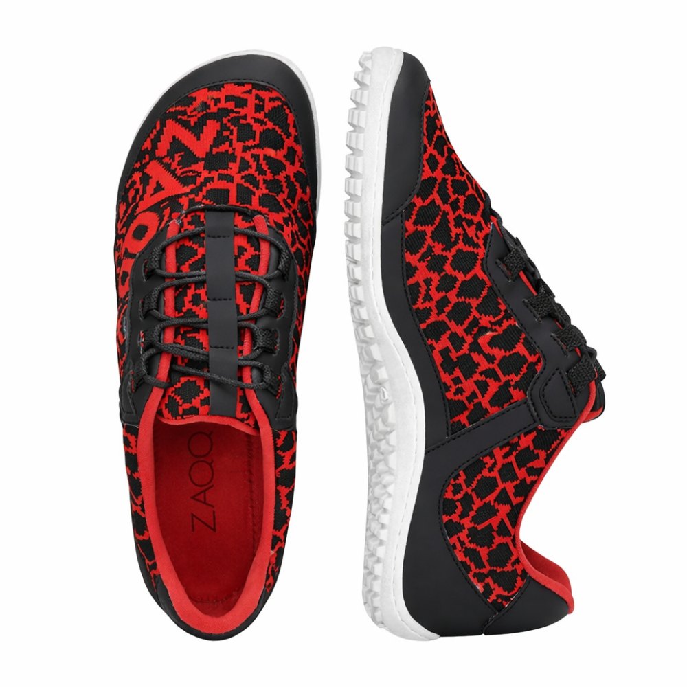 The QASEY Red sneakers from ZAQQ are a pair of stylish vegan barefoot shoes in red, decorated with a black geometric pattern. They feature flexible rubber soles, black laces and a unique tread design. One sneaker is pictured from above while the other is shown from the side to showcase its sleek design.
