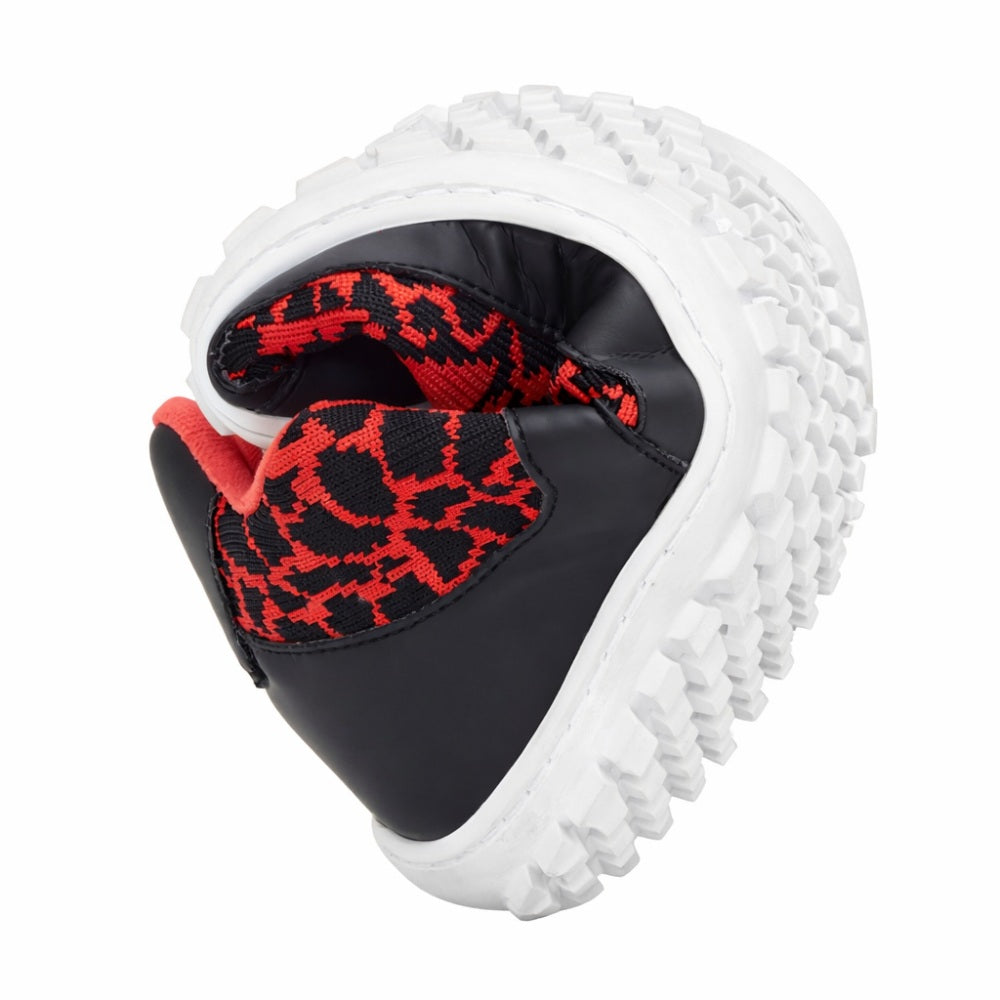 The QASEY Red Sneaker from ZAQQ is curved in the middle, highlighting the flexible rubber sole and showcasing the red and black mesh on the upper. The gray sole with its rough texture emphasizes the flexibility and support of the shoe.