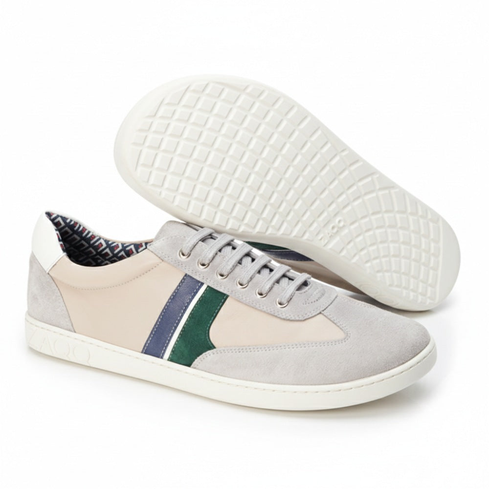 The QLAUDE Gray sneakers from ZAQQ feature beige accents with green and blue stripes, creating an elegant yet casual look. One shoe stands upright while the other shows off its sneaker sole with intricately embossed circular patterns that give this men's barefoot shoe a unique flair.