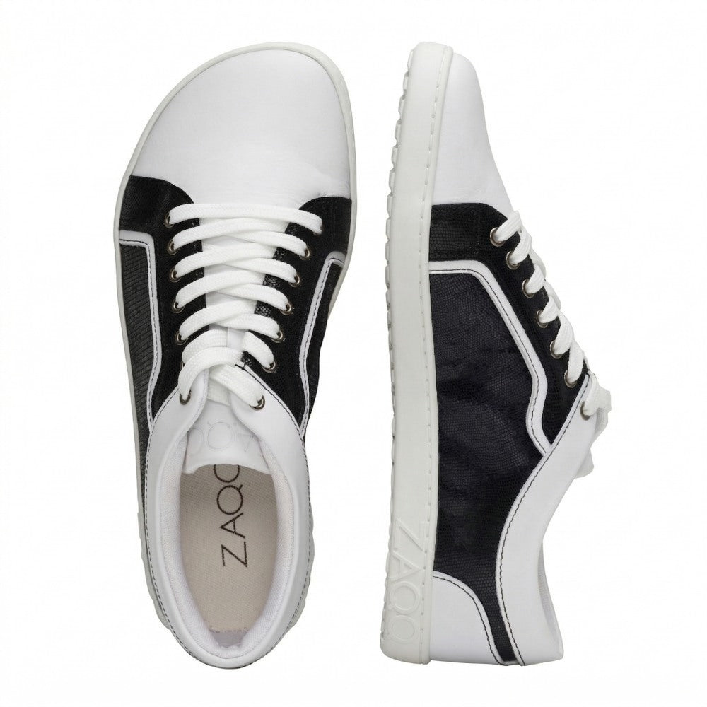 A pair of white QODY sneakers from ZAQQ, in a black and white design with white laces and soles, made from high-quality nappa leather. The brand name is printed on the insole and embossed into the outsole. The shoes are presented with one standing upright and the other lying on its side.