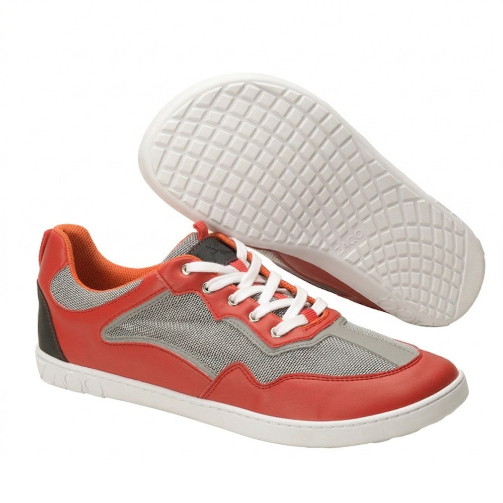 The QOPA Red sports shoes from ZAQQ feature a red and gray upper with white laces and white soles. One shoe stands upright while the other is angled to show the tread pattern. The inner lining is orange for breathability and all-day comfort.