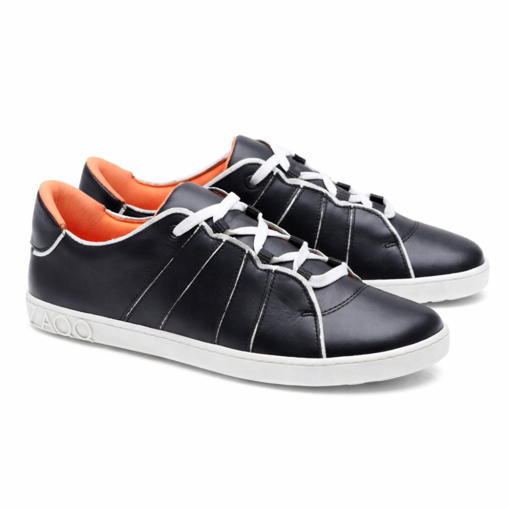 A pair of QQQ Low Black White sneakers from ZAQQ with exceptional comfort, made from black leather with striking white laces and soles. The inside is a bright orange and is highlighted by decorative white stitching on the sides. The shoes are positioned so that they look good from both the side and the front.