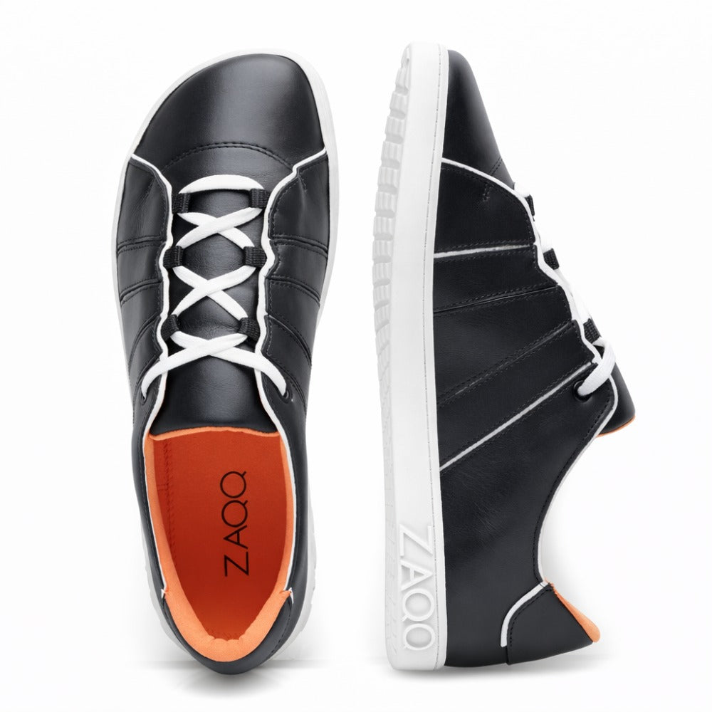 The QQQ Low Black White Sneakers from ZAQQ feature an elegant black leather design with white soles and laces. A shoe is seen from above, showing its red insole and distinctive ZAQQ-Branding while the other can be seen from the side, highlighting its stylish design and comfort.