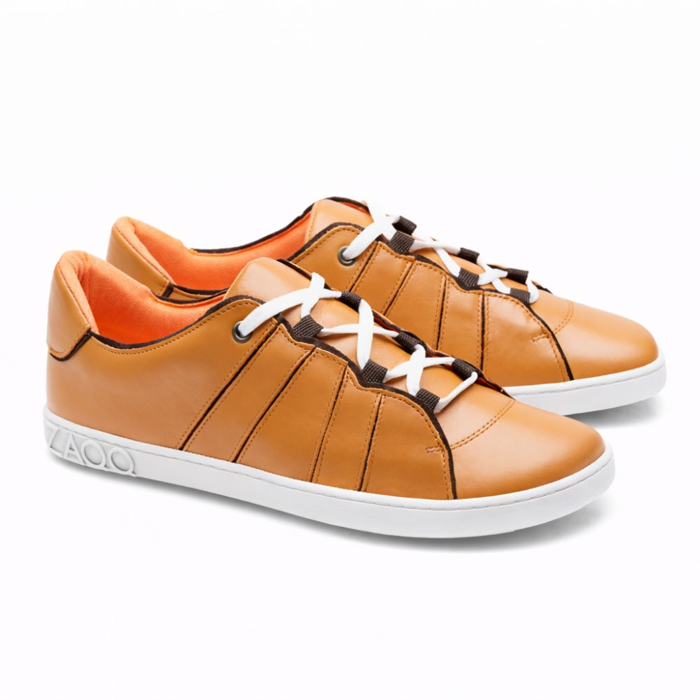 Introducing the QQQ Low Sierra from ZAQQ: A pair of casual sneakers made from light brown nappa leather, complete with white laces and flexible rubber soles. These sneakers feature exquisite brown stitching and a bright orange lining, all of which stand out beautifully against a white background.