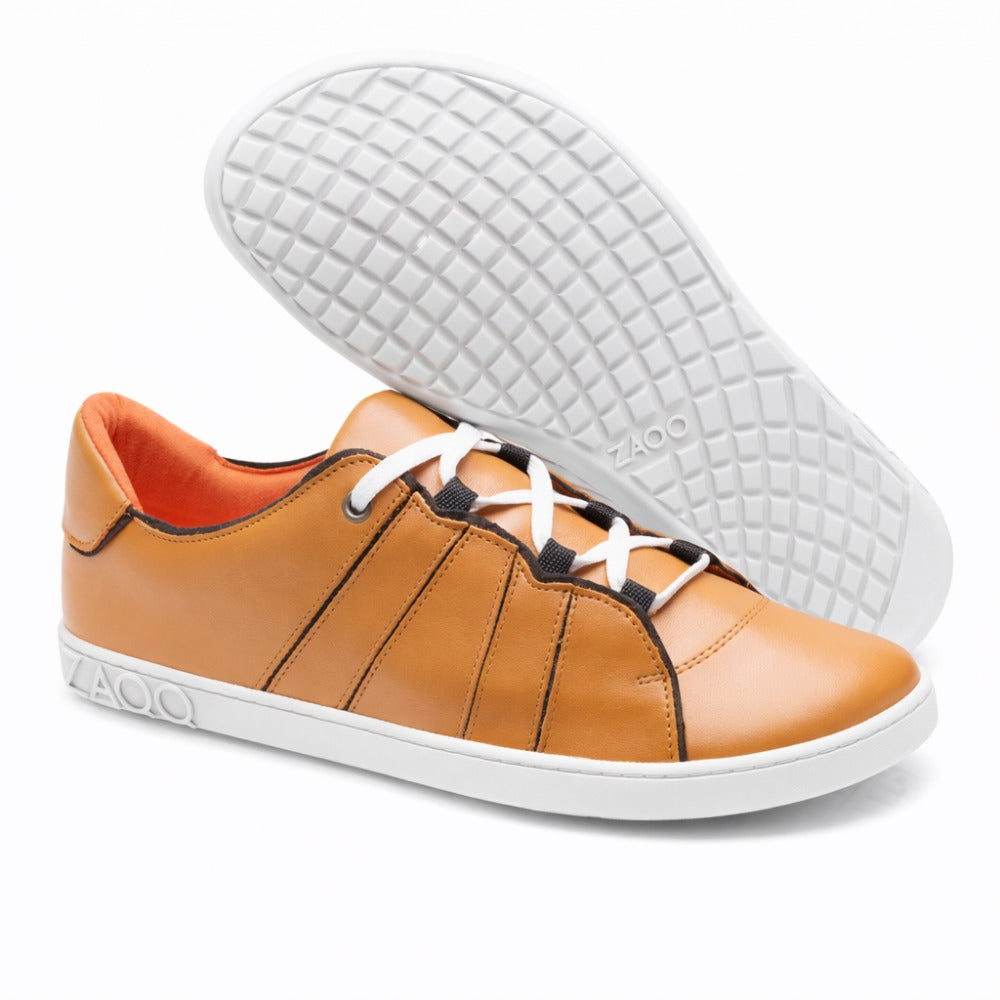 A pair of stylish QQQ Low Sierra sneakers from ZAQQ, in brown nappa leather design with white laces and flexible rubber sole. One shoe stands upright while the other is tilted to highlight its textured sole. The brand name ZAQQ is elegantly placed on the side and sole.