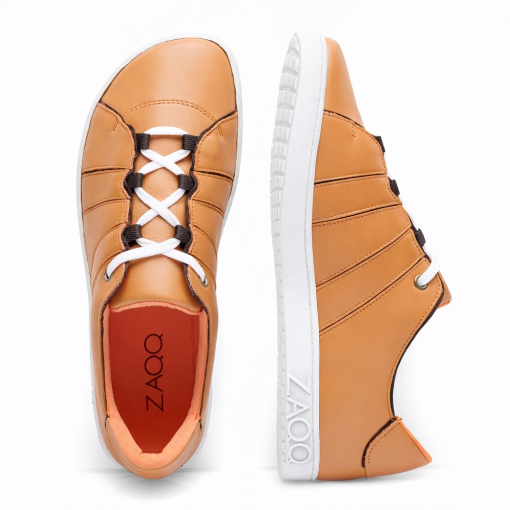 The QQQ Low Sierra from ZAQQ is a pair of light brown leather sneakers made from supple nappa leather. Viewed from above and from the side, these sneakers feature white laces and a thick, flexible rubber sole with the side visible ZAQQ-Branding. The shoes are characterized by a slim design with eye-catching seams.