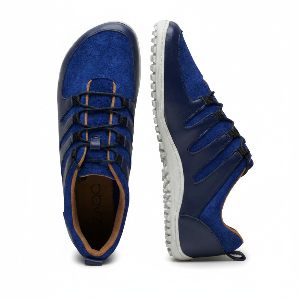 A pair of stylish blue and dark blue SHOQQ Trident sneakers from ZAQQ with white rubber soles. One shoe stands upright while the other lies on its side, showcasing the textured sole pattern and lace-up nappa leather upper.