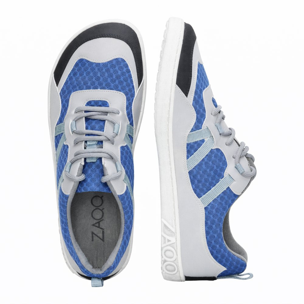 Introducing the SQOTT Blue from ZAQQ – a stylish pair of sporty sneakers in a striking blue and gray color scheme with white soles. One shoe stands upright to beautifully show off its side profile, while the other is positioned to provide a top view. The design includes a unique hexagonal pattern with gray laces that seamlessly combines style and breathable comfort, perfect for your active lifestyle.