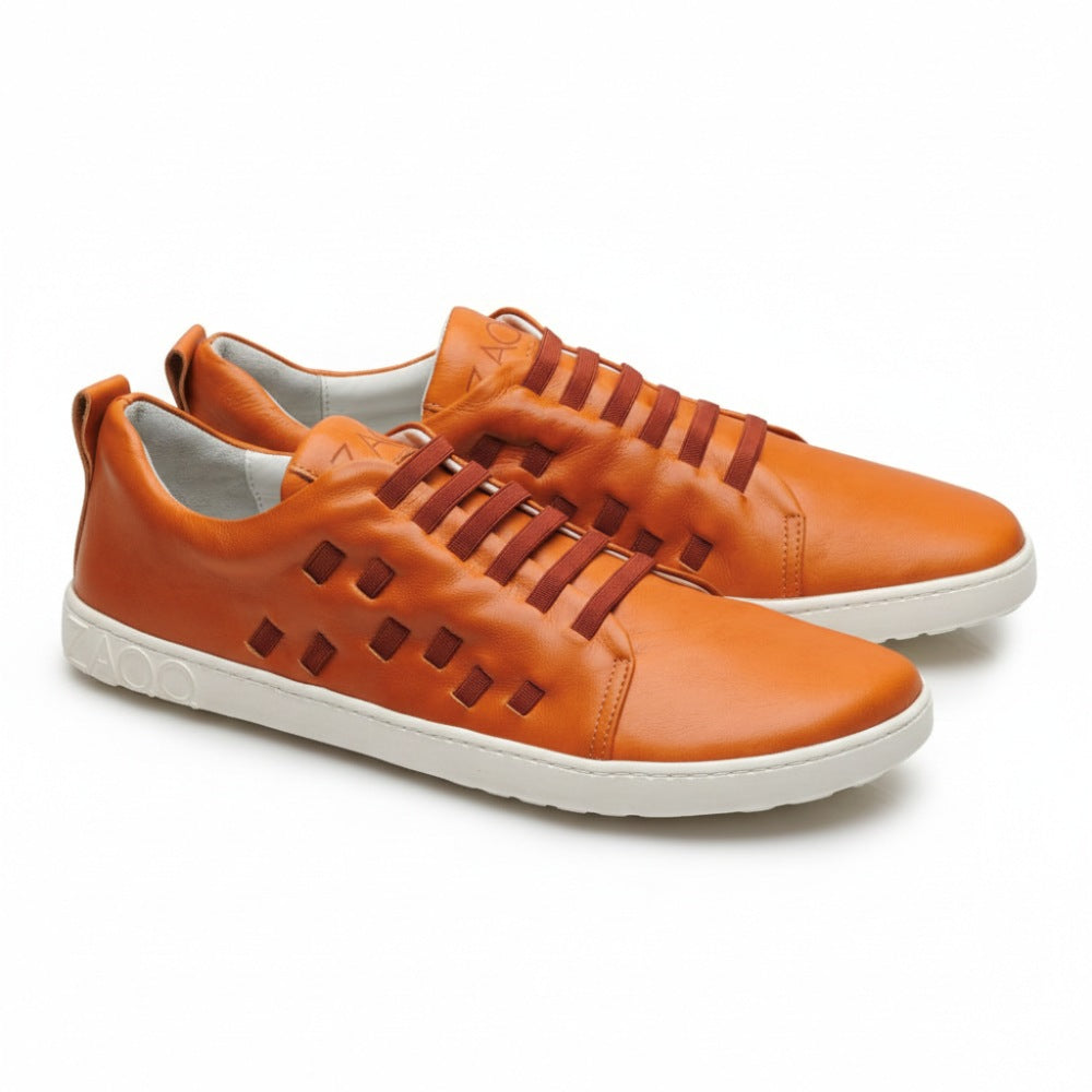 Introducing the STRAQ Sierra from ZAQQ: a pair of stylish orange sneakers made of nappa leather with a white sole. The sides feature square cutout patterns and the brand name ZAQQ is elegantly embossed on the heel. These barefoot sneakers feature a lace-up design with brown laces.